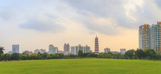 A beautiful panoramic view of tall buildings and Banyan Trees or Liurong temples and a grassy field in the evening against the orange sky in Guangzhou, Guangdong Province, China.