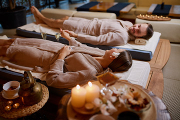 Side view on couple lying down on special beds for massages, after therapy in spa salon