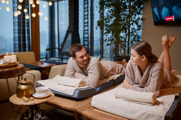 Married young caucasian couple, wife and husband spend time together in spa salon, relaxing, look at each other and smile, happy after beauty treatment