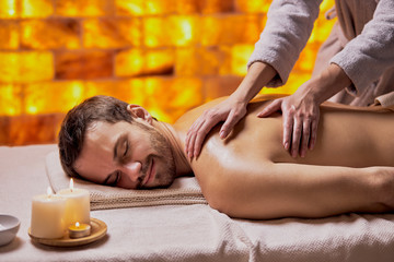 Obraz na płótnie Canvas Handsome caucasian man getting massage in the beauty salon, spa salon, naked skin. Young bearded man relaxing,yellow wall background in spa