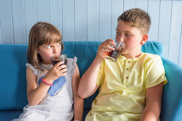 Children drink sweet water sitting on the couch.
