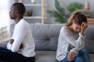 Stressed irritated young mixed race couple sitting separately on couch.
