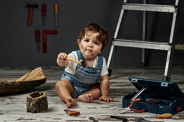 A baby playing with work tools and wood in a workshop