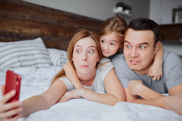 let's take selfie, photo. portrait of beautiful funny family taking selfie with daughter, kid girl wearing casuals on bed at home