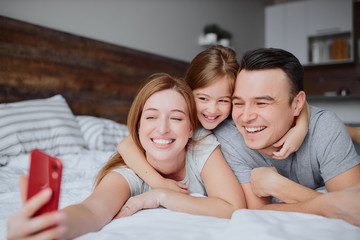Obraz premium happy caucasian parents lying on bed together with kid girl, having leisure time together at home