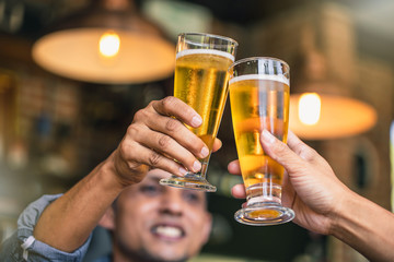 Happy friends drinking and toasting beer at brewery bar restaurant. Friendship concept with young people having fun together at cool vintage restaurant.