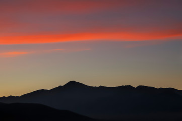 scarlet stripe of clouds in the dark sky, purple silhouettes of a mountain range in the distance - alpine landscape at sunset, Mongolia