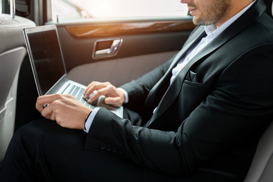 unrecognizable man wearing tuxedo use laptop in luxurious car, working. side view