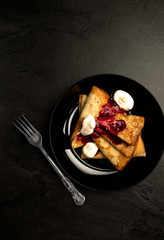 Thin pancakes with sugar powder and berries in a black round plate on a dark background .
