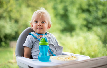 Cute baby sitting in high chair at the dinning table outdoor