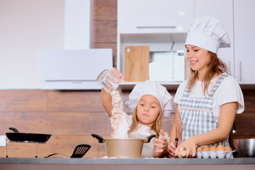 enjoy baking and cooking with mother. litttle girl sprinkling flour from cap before baking cake, using chicken eggs