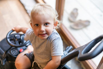 Cute little baby boy sitting in small toy car at home