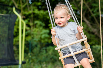 Cute little boy playing on swing in backyard at coutryside