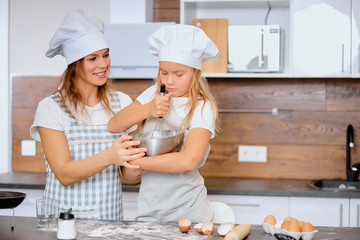 caucasian child making dough with the use of mixer with mother in kitchen at home, use chicken eggs and flour . Prepare ingredients for baking