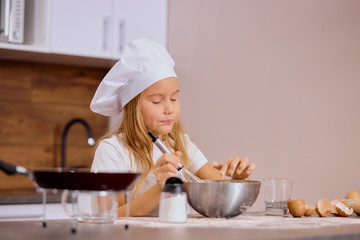 careful caucasian little girl try to bake independently in kitchen, mixing dough in bowl, happy to bake or cook