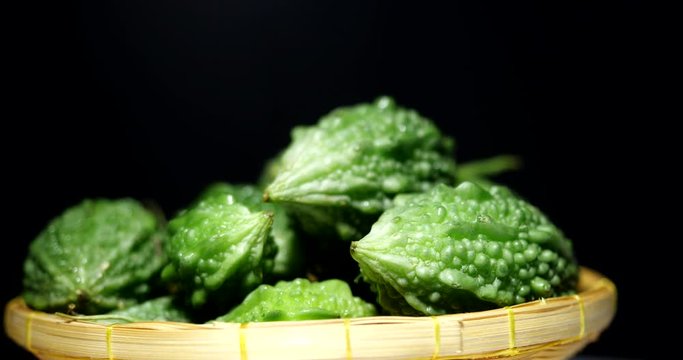 Green bitter gourd with water drops. Whole green bitter melons rotating on black background. 4K resolution