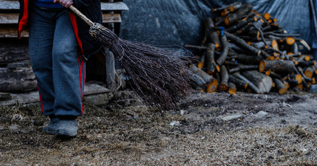 Obraz premium Cleaning in the yard in late fall, a woman with a broom cleans her yard.
