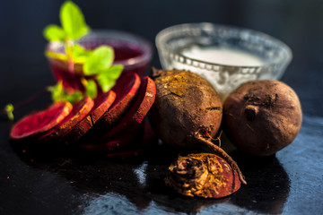 Beetroot face mask on the black glossy surface consisting of some grated beetroot vegetable and sour cream well mixed in a glass bowl along with raw cut sliced beetroot vegetable and cream.