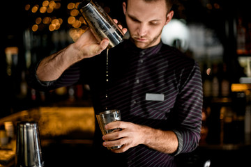 Male bartender pouring a cocktail drink from the one half of the steel shaker to another