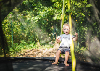 Little child playing and jumping on trampoline outdoor in backyard