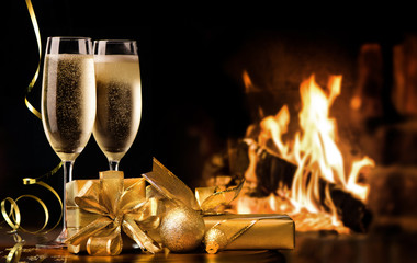 Two champagne flutes with gold gift boxes and streamers in front of fireplace