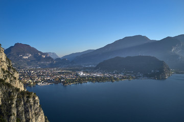 Fototapeta na wymiar Steep cliff, view of the city of Riva del Garda, Italy. Panoramic view of Lake Garda in the foreground, the city is surrounded by rocks and alpine mountains. Autumn season.