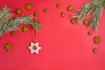 A Christmas toy made from homemade gingerbread cookies in the form of a snowflake sprinkled with icing sugar hanging on a pine branch with hoarfrost. Flat lay on red background with copy space.