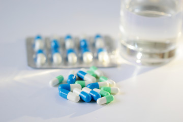 Medicine blue,white and green capsules with water glass on white background.