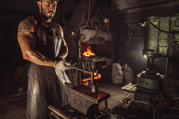 Fototapeta na wymiar muscular skillful forger at workshop wearing leather apron isolated in dark space, furnace in workshop
