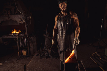 Fototapeta na wymiar young blacksmith heating hot red metal for future manufacturing in workshop. forging industry