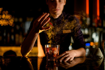 Professional bartender drop an essence to a a glass with cocktail with ice in the smoke