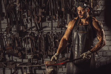 Plakat young muscular blacksmith man manually forging the molten metal. Blacksmith hammering hot metal arrow blade, wearing leather apron