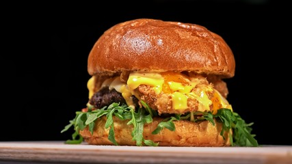 Craft burger is cooking on black background in black food gloves. Consist: sauce, arugula, tomato, red onion rings fries, cucumber, cheese, air bun and marble meat beef. Not made ideal. Looks real