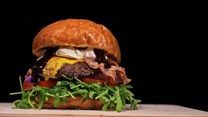 Craft burger is cooking on black background. Consist: sauce, arugula, tomato, red onion, bacon, red...