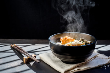 Noodles with steam and smoke in bowl on wooden background, selective focus. Asian meal on a table, junk food concept