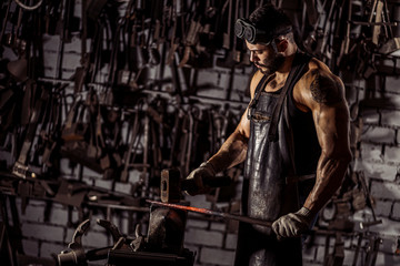 Fototapeta na wymiar young muscular blacksmith man manually forging the molten metal. Blacksmith hammering hot metal arrow blade, wearing leather apron