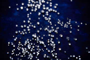 Abstract bokeh pattern of sparkling glass droplets on a dark blue background