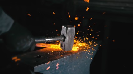 Forge workshop. Smithy manual production. Hands of smith with hammer hit on glowing hot metal, on...