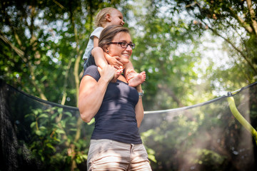 Little child with his mom playing on trampoline outdoor in backyard