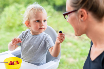 Mother and her baby son eating together outdoor and have fun