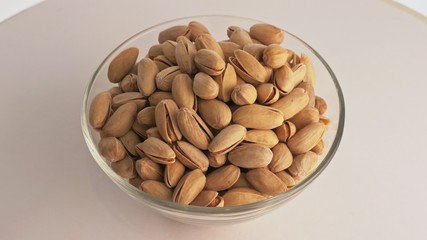 Nuts pistache rotate are on a table in a plate. Snack in transparent dish on an isolated white background are spinning moving. Delicious and healthy protein-rich diet food.