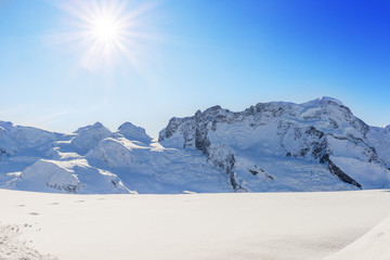 Mountain panorama with fresh snow, blue sky and sun with rays. Rocks sprouting from the snow, Christmas time, nativity scene.