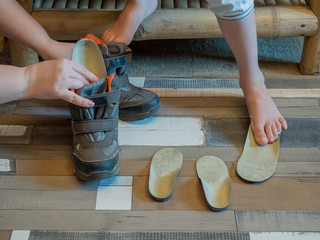 Beautiful bare children's feet with therapeutic orthopedic insoles for shoes on a wooden parquet background. Flatfoot treatment. Closeup of little male barefoot legs