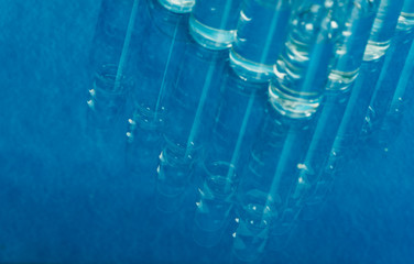 Glass medical ampoule vial for injection. Medicine is liquid sodium chloride with of aqueous solution in ampulla. Close up. Bottles ampule multicolor on background color and water. Human plasma.