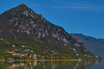 Panoramic view of the mountains and Lake Idro. Autumn season, the reflection in the water of the mountains, trees, blue sky