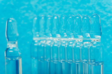 Glass medical ampoule vial for injection. Medicine is liquid sodium chloride with of aqueous solution in ampulla. Close up. Bottles ampule multicolor on background color and water. Human plasma.
