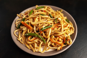 Asian vegetarian food udon noodles with Beijing cabbage, carrots, green beans, bell pepper, onions on a plate on a stone background