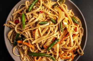 Asian vegetarian food udon noodles with Beijing cabbage, carrots, green beans, bell pepper, onions on a plate on a stone background