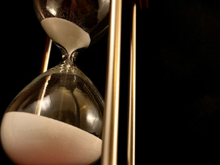 Hourglass on a stand, black background. Glass hourglass in the case. Glass time meter. Concept:...