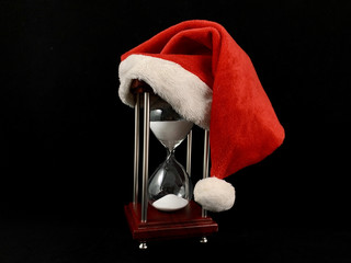 Hourglass in the cap of Santa Claus. Christmas hat on glass hourglass. Glass device for measuring...